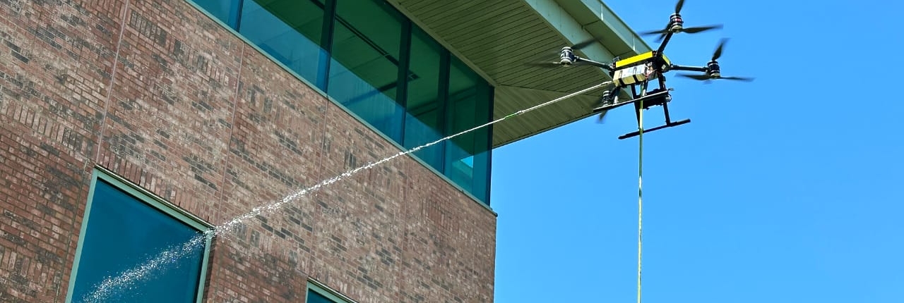 A drone pressure washing the side of a tall building.